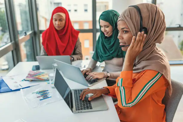 Three interpreters wearing headsets working together at laptops in a bright office